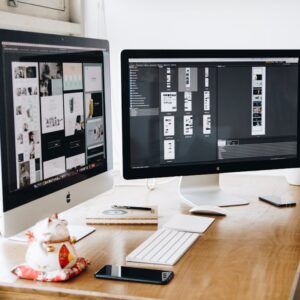 Two Imac's With Keyboard and Phones on Desk